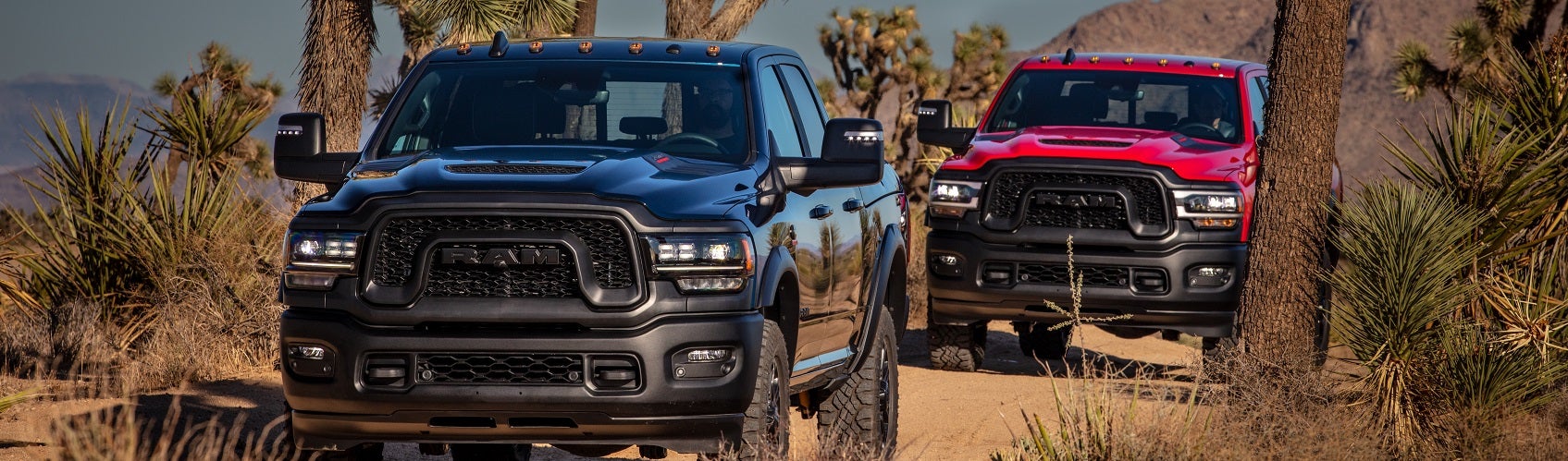 Two RAM trucks driving on a dirt road in the desert
